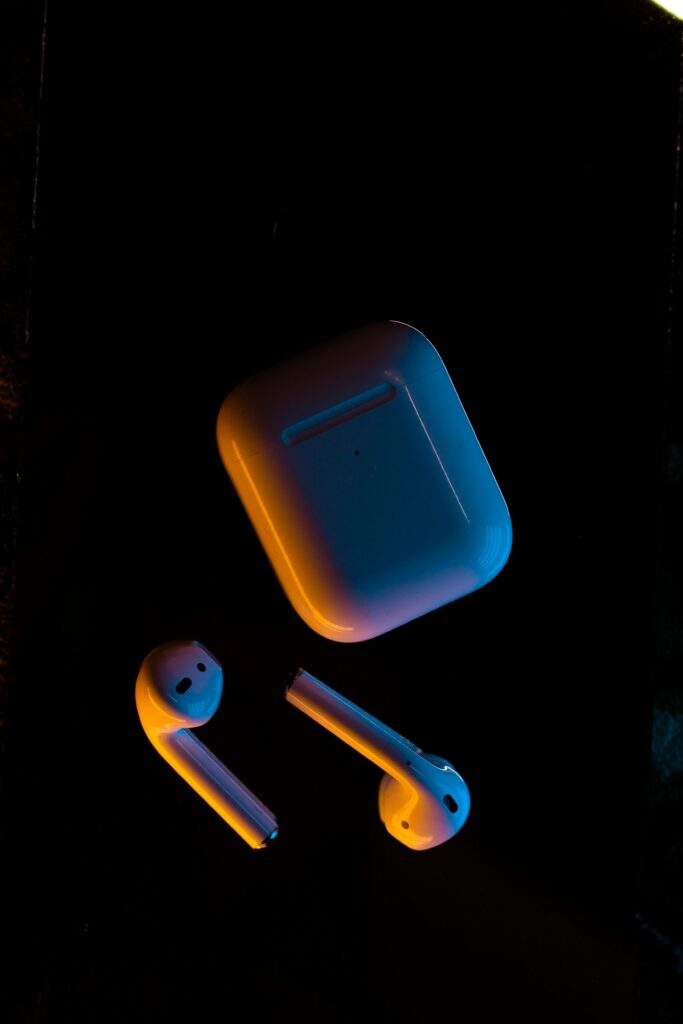 Modern wireless earbuds with a warm glow, isolated on a dark surface.